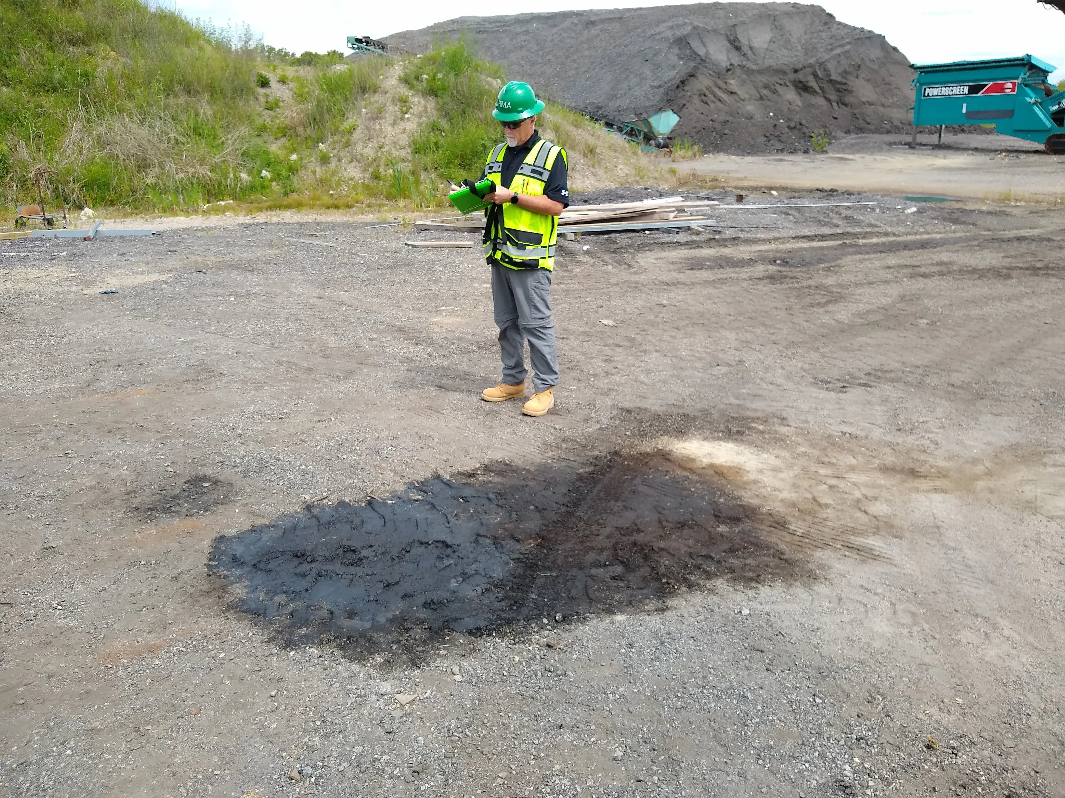 RMA environmental consultant taking notes near a surface stain during a Phase I Environmental Site Assessment