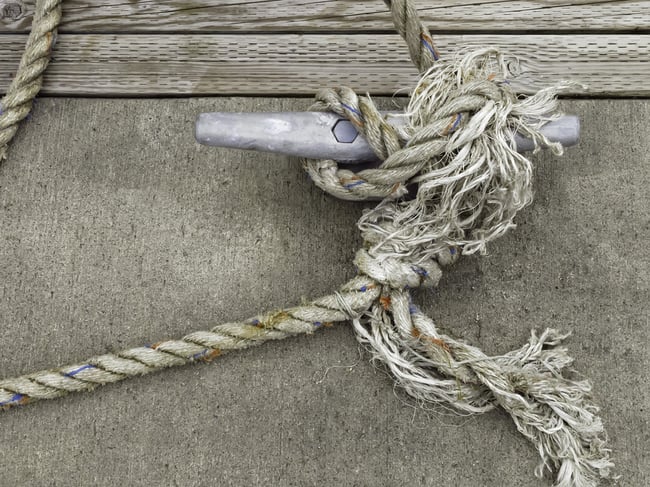 Frazzled line holding a boat to a cleat on dock in marina